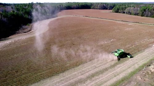 Drone footage of soy bean harvesting on a farm field with a harvester or tractor, rotating aerial sh