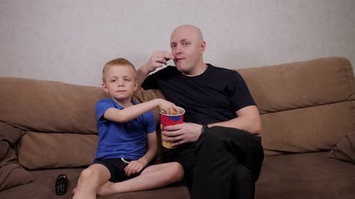 Boy and Man Eating Popcorn on Couch Together