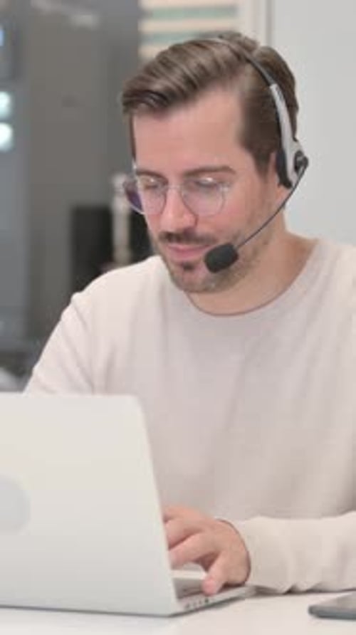 Young Man with Headset Doing Video Chat on Laptop in Call Center