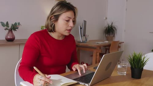 Young Woman Works on Laptop and Writes Notes