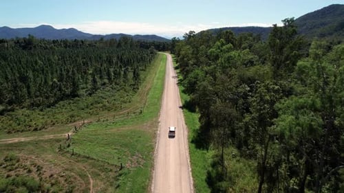 drone shot of a campervan driving on a gravel road in Queensland countryside with mountains in the b
