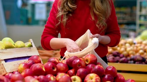 Mujer recogiendo manzanas en una bolsa reutilizable en una tienda. Temáticas del Día de la Tierra y la Ecología