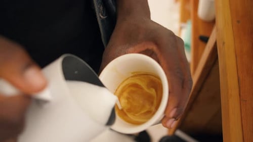 Close up of Barista's hands pouring steamed milk into white mug and creating latté art behind counte