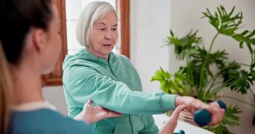 Elderly woman with weights for exercise with physiotherapist at physical therapy clinic
