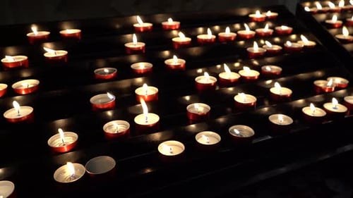 Candlelight in Dark Rows of Votive Candles Burning in a Church