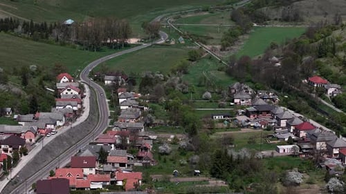 An elevated view captures a rural village with its winding road through a green valley, surrounded