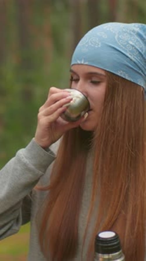 Young Woman Enjoying Warm Drink From Thermos in Peaceful Forest
