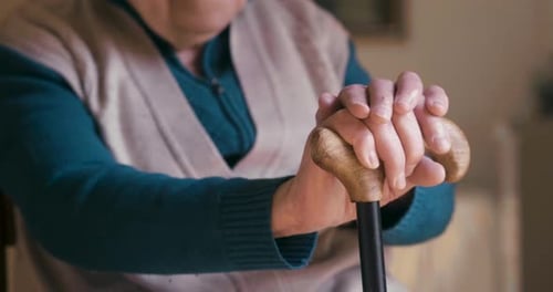 Authentic close up shot of smiling disabled senior woman with a stick is looking outside a window.