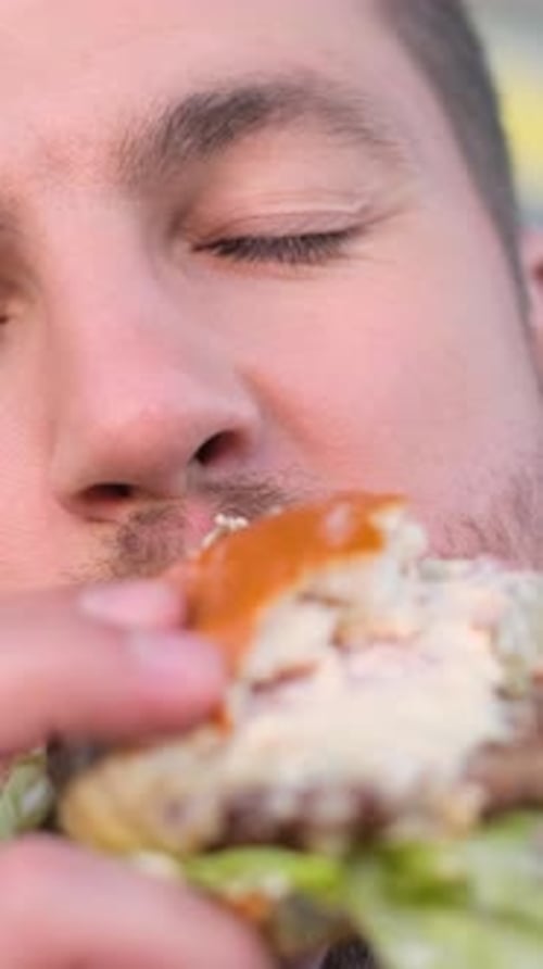 A Man with a Beard is Eating a Hamburger with His Eyes Closed