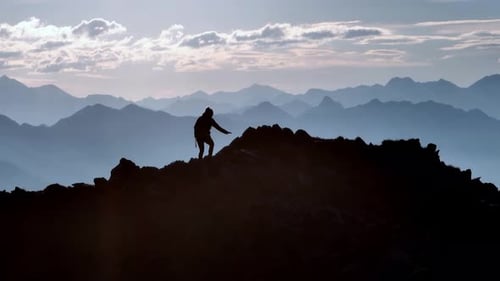 Female mountaineer walking on a ridge backlit by the sun and other mountains in the background