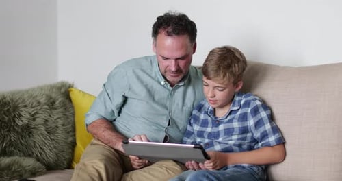 Father and Son Using Tablet on Sofa at Home
