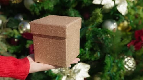 Frau in Nahaufnahme zeigt festliche goldene glitzernde Schachtel mit Weihnachtsgeschenk