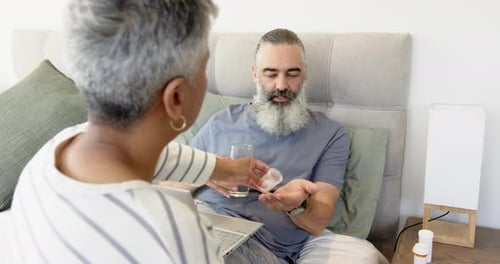 Woman Gives Man Pills and Glass of Water in Bed
