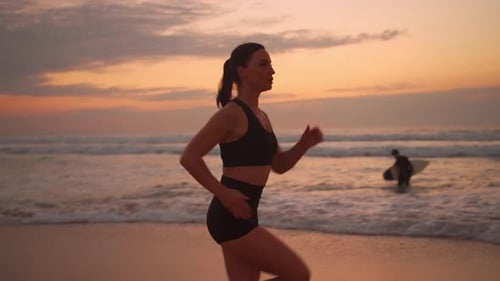 Athletic Woman with Waving Hair Running on Beach at Dramatic Sun Background