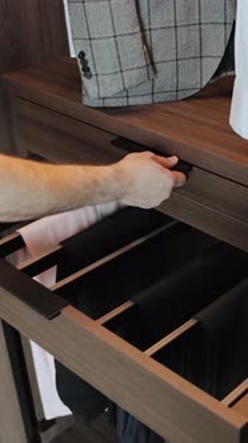 Closeup of a Man's Hand Opening a Wardrobe Drawer to Access Neatly Folded and Organized Clothes