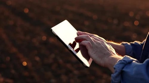 Cropped shot of male farmer's hands use digital tablet on plowed field for control of soil quality,