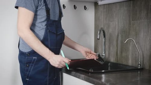 An Unrecognizable Plumber Checks the Condition of the Plumbing and Kitchen Faucet in a Residential