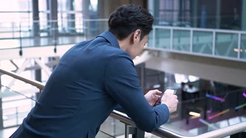 Mature businessman text messaging on smart phone at office atrium railing