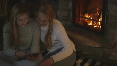 Young women using digital tablet in chalet, fireplace in background