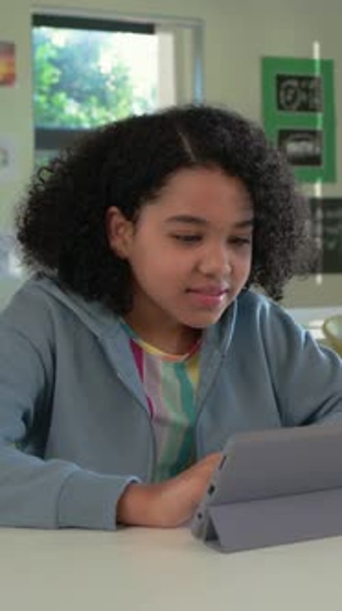 Vertical video: Seeing screen, student in hoodie leaning to view, tapping tablet at classroom desk