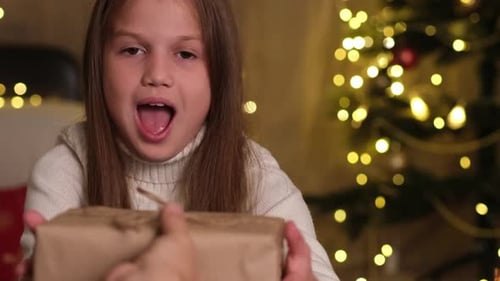Happy Kid Girl Receiving Christmas Gift Box From Parents in Decorated Room