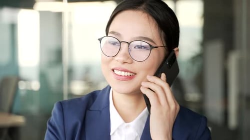 Confident young asian businesswoman talking on phone sitting at workplace in business office. Busy