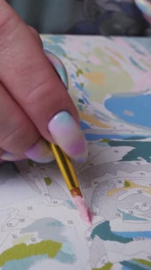 The young woman paints a picture by numbers with paints with a brush, in motion, close-up. Vertical