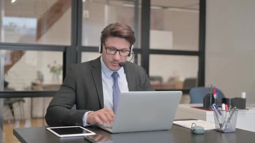 Call Center Man Working on Laptop while Sitting with Headset