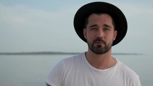 Man wearing hat on beach looking at camera