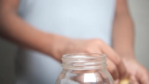 Coins Dropped into Glass Jar for Savings