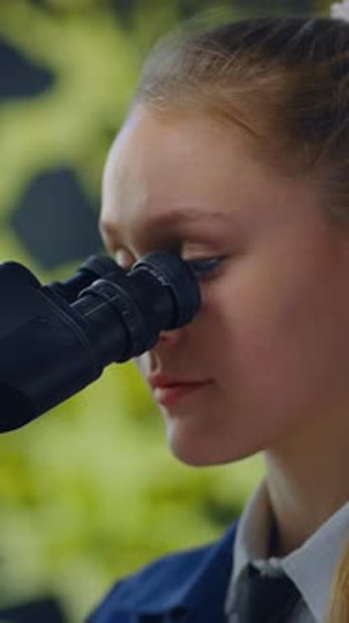 Teenage Girl in Lab Coat Looks Through Microscope