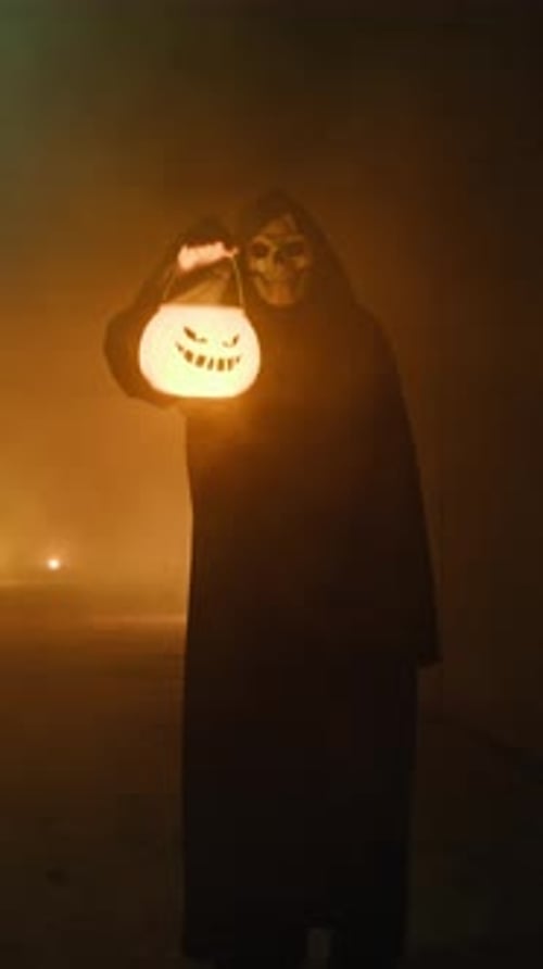 Figure in Skull Mask Holds Jack-o-Lantern