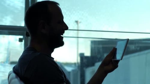 Silhouette Of Man Watching Movie On Tablet Sitting In Lobby At Airport