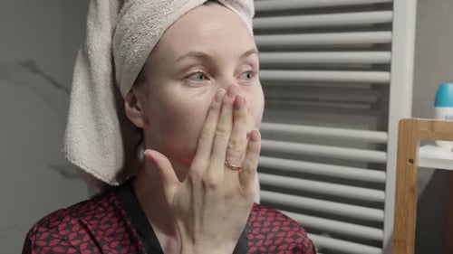 Woman Applying Skincare Product on Face in Bathroom