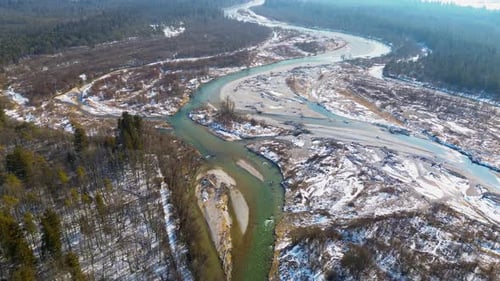 Aerial view of a winding river flowing through a snow-covered landscape with sandbanks, bare trees,