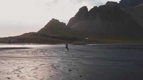 Person Walking on Reflective Black Sand Beach in Iceland