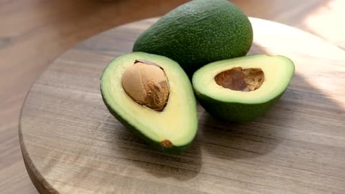 Whole And Half Avocado Rotating On A Wooden Plate
