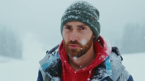 Portrait of Handsome Young Bearded Man in Green Knitted Hat Standing Looks at Camera in Snow Winter