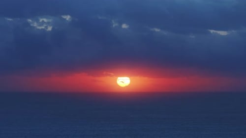 Puesta de sol sobre el océano con nubes rojas y azules vívidas en el horizonte