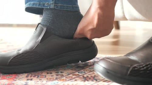 Person Putting on Brown Leather Shoe Indoors