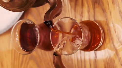 Das Mädchen gießt türkischen aromatischen Tee in ein traditionelles Glas. Tee aus zwei Teekannen wird in eine