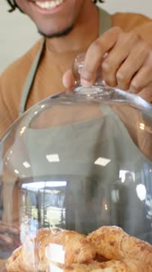 Vidéo verticale : Atteignant le bouton de la cloche, un homme en tablier soulevant une cloche au café présentant des pâtisseries