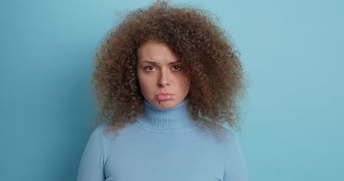 Woman with curly hair and sad expression on blue