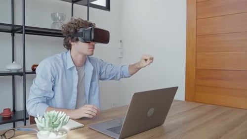 Man Uses VR Headset at Desk with Laptop