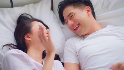 Asian new marriage couple lying down on bed and looking at each other.