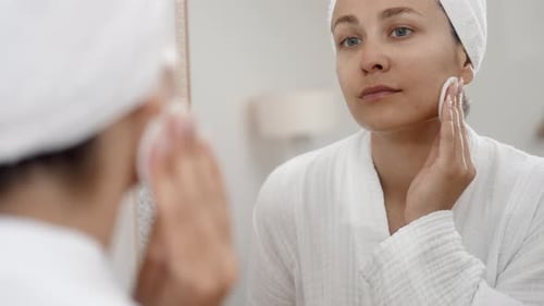Woman Cleans Face in Mirror with Cotton Pad