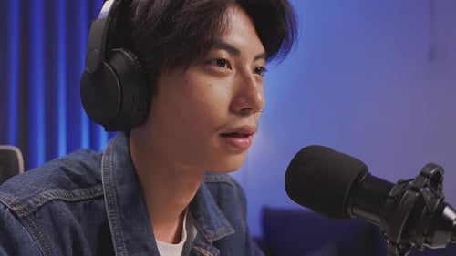 Close up of young Asian content creator speaking into microphone during podcast session