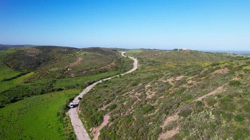 Vehicles Driving On Winding Road Along The Mountain Towards The Sea. - aerial shot