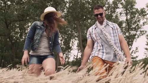 Young couple in love laughing and walking through a grassy field on a windy day