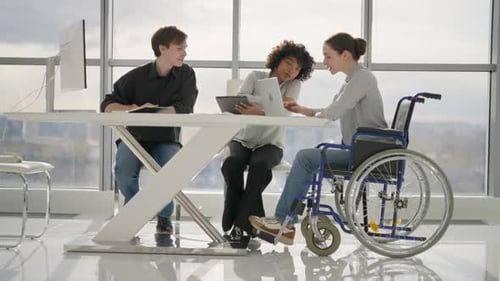 Woman in Wheelchair Discussing Working Project with Colleagues in Office Sitting at Table Looking at